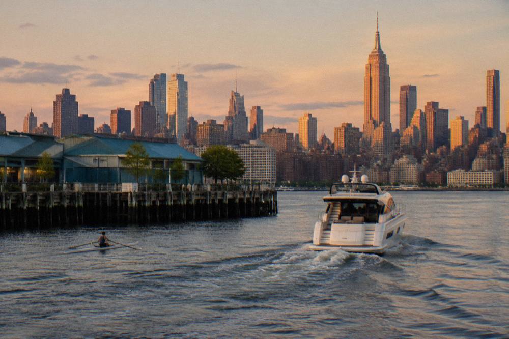 A small motor yacht cruising on the Hudson River with Midtown Manhattan skyscrapers glowing in evening light