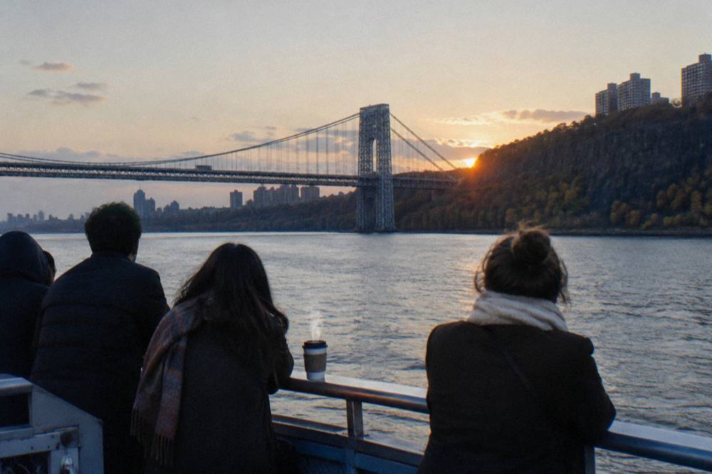 Passengers at the rail of a sightseeing boat watching the sun drop behind the New Jersey skyline
