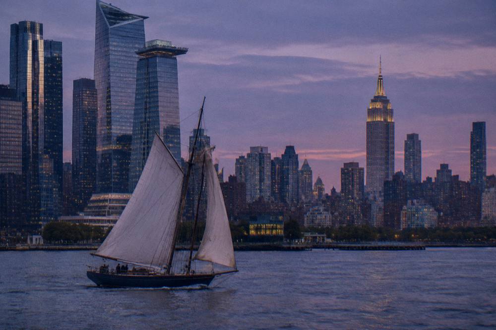 A schooner under full sail on the Hudson at dusk with the Empire State Building behind it