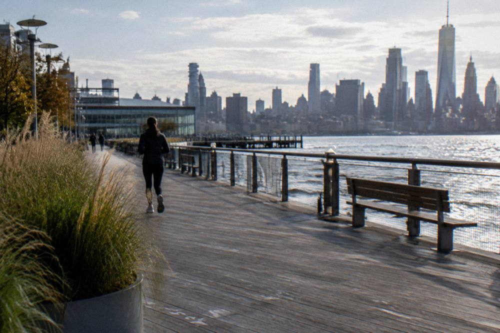 A waterfront promenade along the Hudson River with the Manhattan skyline behind it